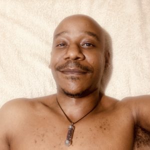 medium photo of ndlela shirtless, smiling, wearing a garnet pendant