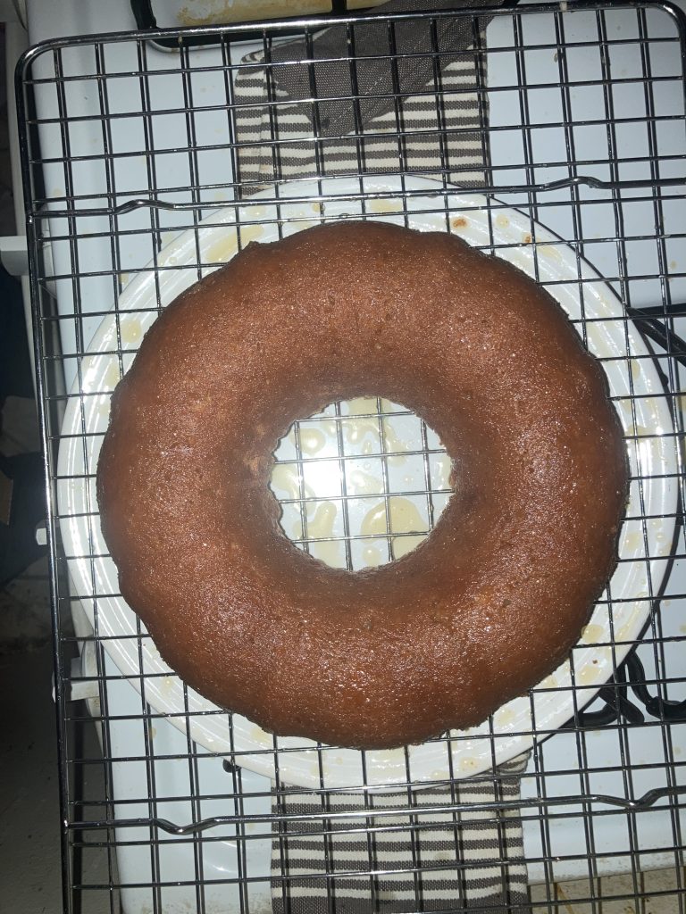 Top view of a whole lemon pound cake on a wire rack sitting on a white plate on a white stove.