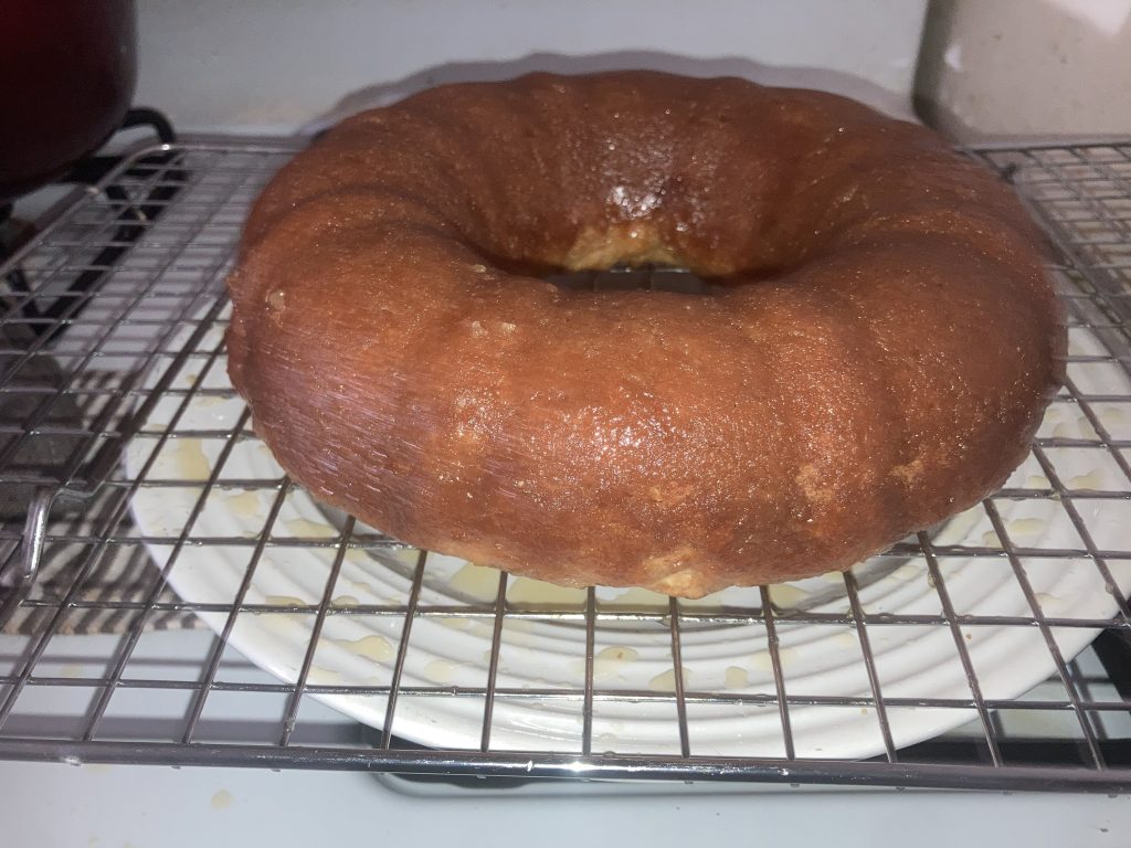 Side view of a whole lemon pound cake on a wire rack sitting on a white plate on a white stove.