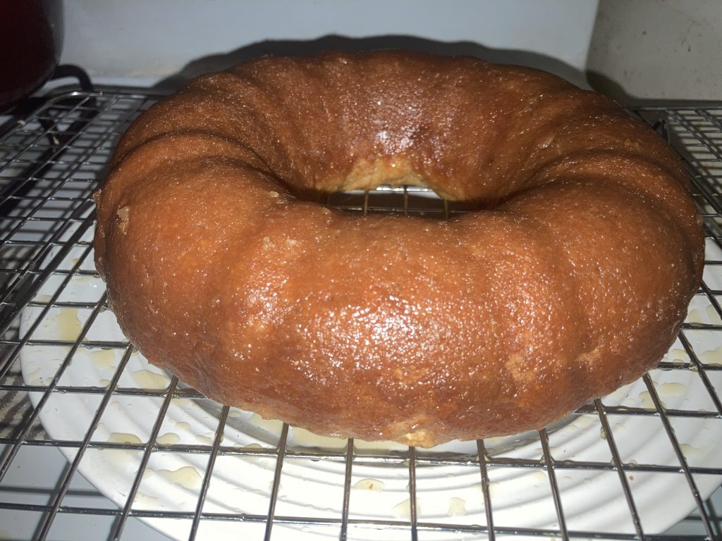 Side view of a whole lemon pound cake on a wire rack sitting on a white plate on a white stove.