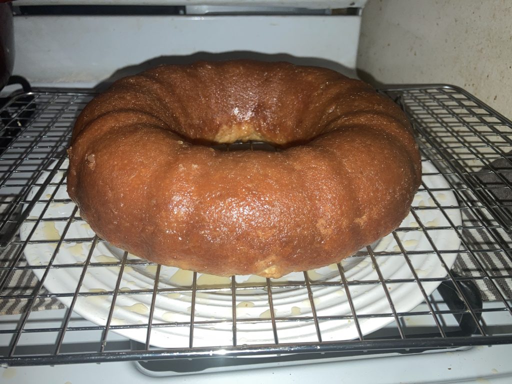 Side view of a whole lemon pound cake on a wire rack sitting on a white plate on a white stove.