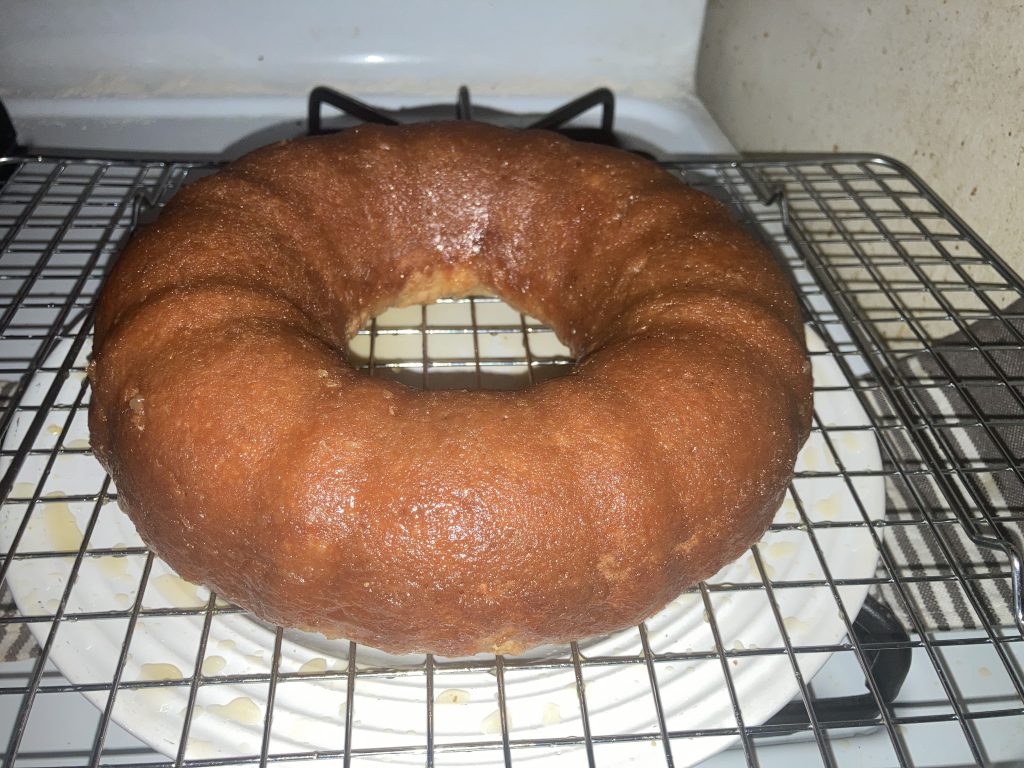 Side view of a whole lemon pound cake on a wire rack sitting on a white plate on a white stove.