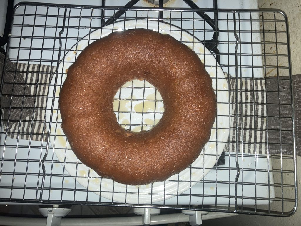 Top view of a whole lemon pound cake on a wire rack sitting on a white plate on a white stove.