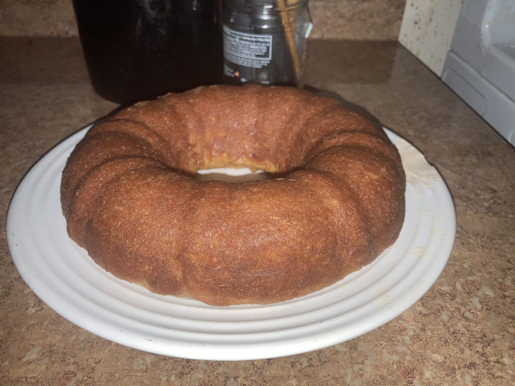 Side top view of a whole lemon pound cake on a white plate on a kitchen counter.