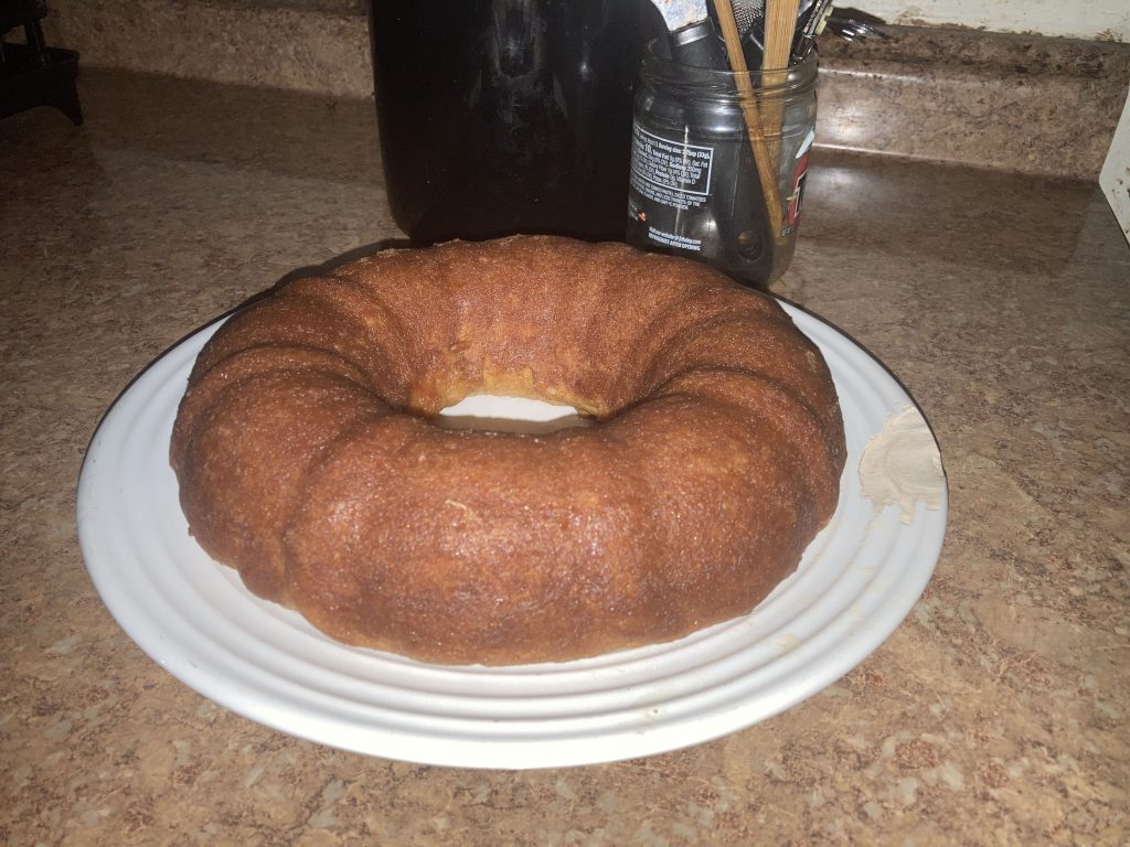 Side top view of a whole lemon pound cake on a white plate on a kitchen counter.