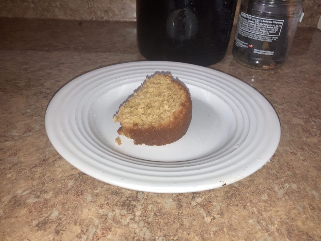 Side top view of lemon pound cake slice on a white plate on a kitchen counter.